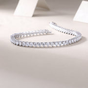 A tennis bracelet featuring round-cut moissanite stones set in a row on a silver metal band, displayed against a neutral background.